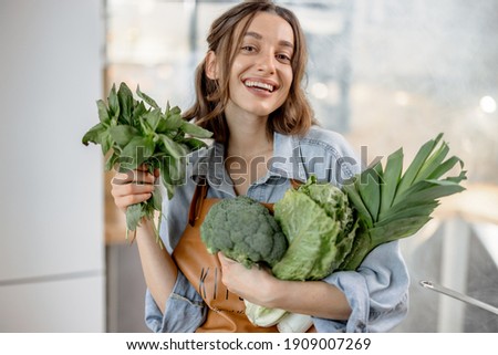 Portrait of pretty smiling woman with fresh broccoli, roman salad, basil on the kitchen with steam on background. Healthy green vegetable concept. Close up. High quality photo