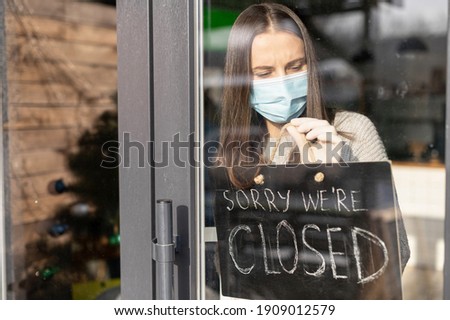 Frustrated female cafe or store owner wearing medical mask hangs a sign board with an inscription sorry we are closed, small business lockdown due to coronavirus, bankrout concept