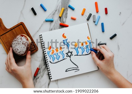 A girl drawing a celebration card with menorah (traditional candelabra) and candles for Happy Hanukkah jewish holiday. 