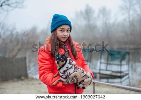 Girl 10 years old. TTeenager girl in orange jacket, hat and scarf. Girl and chihuahua. Dog