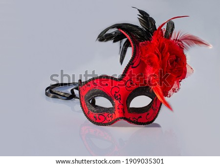 Red carnival mask with feathers, isolated on gray background with shadows.