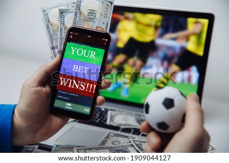 Smartphone with betting mobile application and male's hand with soccer ball. Sport and betting concept Royalty-Free Stock Photo #1909044127