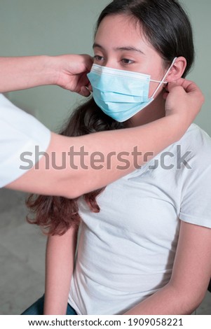 Female doctor placing a mask on a Latina teenager as a means of preventing contagion