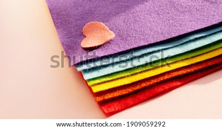 A felt heart rests on a stack of fabric folded in the colors of the LGBT flag. LGBT day concept.