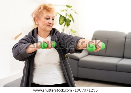 Closeup portrait of active senior woman doing dumbbell exercises at home, smiling.