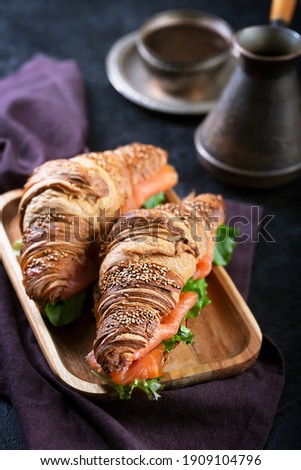 Croissant Sandwich with salmon and salad leaves on a dark black table
