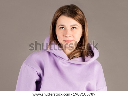Photo of european woman, concentrated above and ponders about something, poses against gray background, empty space for your promotion or information
