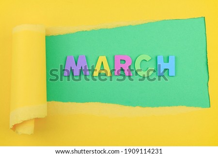 The word March on a green background with torn yellow paper on top, close-up.