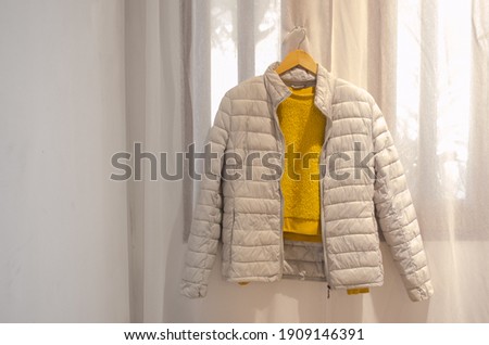 Gray jacket and yellow sweater hanging on a wooden hanger on light background. Trendy colors clothes.
