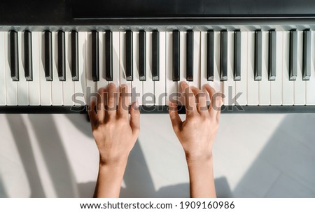 Piano learning chords at home - woman playing digital keyboard with online music lesson. Top view of musician hands on keys. Royalty-Free Stock Photo #1909160986