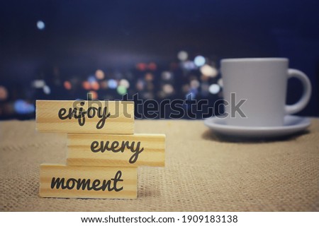 Selective focus image of wooden tiles with text ENJOY EVERY MOMENT and cup of coffee. Bokeh effect background