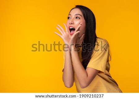 Surprised happy beauty asian woman looking copy space in excitement Expressive facial expressions Presenting some product Beautiful girl act like a telling customer Isolated on yellow background