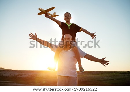 Dad and son launch a plane at sunset in summer
