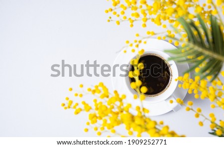 a spring bouquet with yellow mimosa flowers over a cup of black coffee on a white table. concept of 8 March, happy women's day. Top view and copy space
