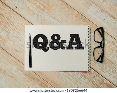 Top view text Q and A written on notebook with pen and eye glasses on wooden table. Q and A concept.