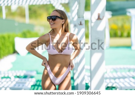 Beautiful young woman in bikini relaxing on chaise lounge near swimming pool