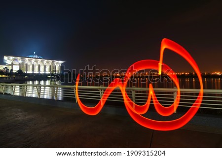 Light painting of word “Allah” (English translation God) with mosque on the lake with reflection. Image taken using infinity focus to produce long exposure light painting