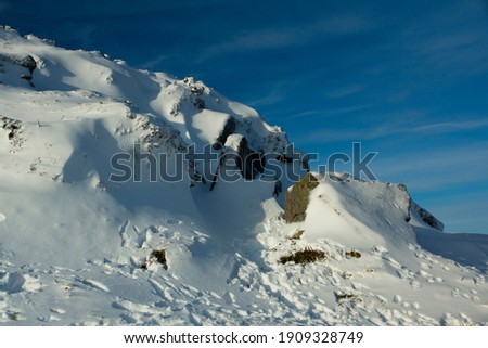 A landscape image of bright white snow covered rocks to the left of picture with an almost clear blue sky beyond.