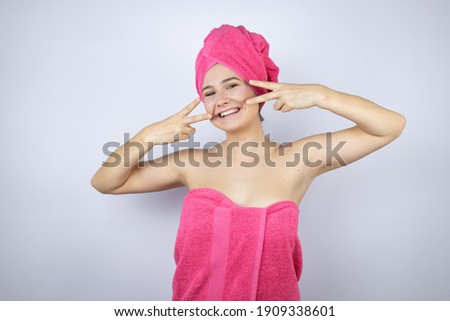 Young beautiful woman wearing shower towel after bath standing over isolated white background Doing peace symbol with fingers over face, smiling cheerful showing victory