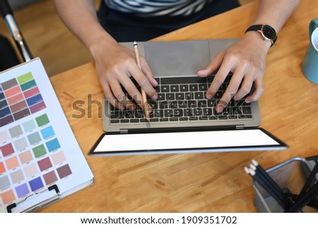 Overhead shot of young man designer working with laptop computer and color swatches on wooden table.