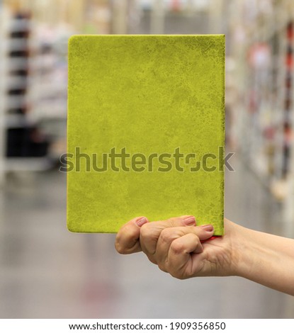 The hand holds a green notebook. A place for your advertising, drawing, lettering. Blurred background