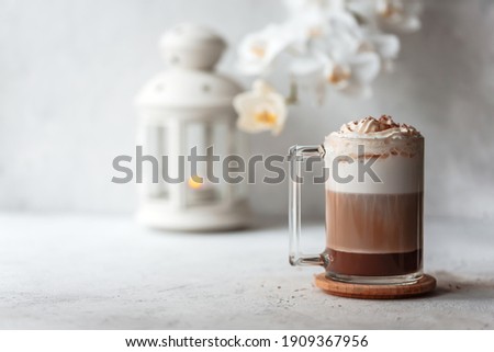 Hot latte macchiato with delicious foam in a tall transparent glass on an easy table setting. Photo in a high key. Breakfast time. Rustic background.