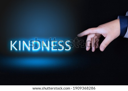 KINDNESS text, word written in neon letters on a black background pointed to by a hand with a person's index finger.
