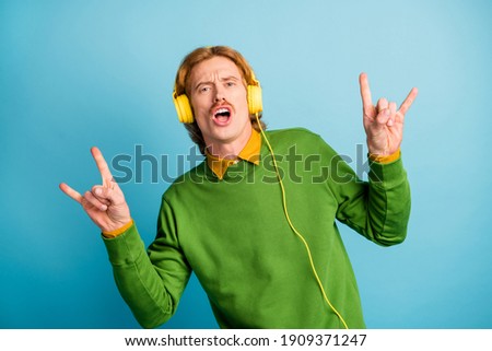 Photo of young funky funny cool man in headphones showing rock n roll sign isolated on blue color background Royalty-Free Stock Photo #1909371247