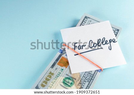 Text written note FOR COLLEGE with dollars cash money in rubber band, on copy space blue background - concept of financial planning to save money for purpose of education