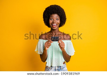 Photo portrait of excited woman holding credit card in two hands isolated on vivid yellow colored background