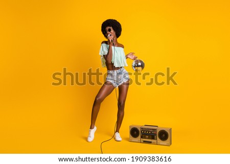 Full length body size photo of black skinned girl singing with boombox microphone wearing shorts top isolated on bright yellow color background