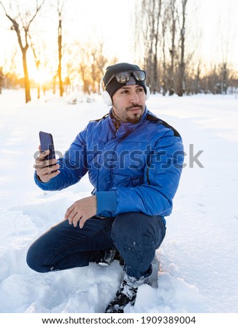man with headphones and smartphone listening music happy smiling, wearing winter clothes in snow