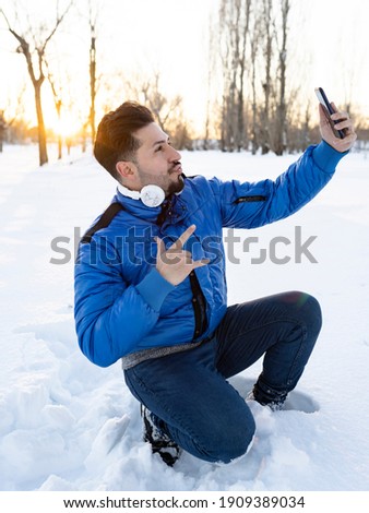 handsome smiling man in casual clothes makes selfie with his smartphone in the snow