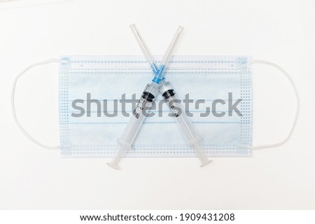 vaccination concept: two syringes with vaccine crossed out medical mask on white background