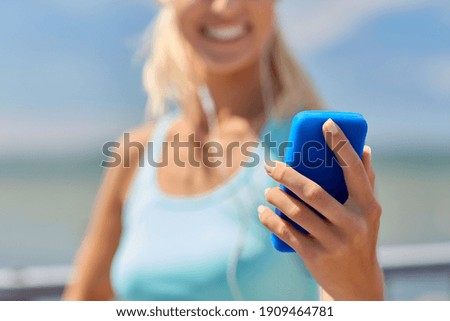 sport, fitness and technology concept - close up of happy smiling sporty young woman with smartphone and earphones