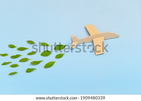 Wooden airplane model emitting fresh green leaves on blue background. Sustainable travel; clean and green energy; and biofuel for aviation industry concept. Royalty-Free Stock Photo #1909480339