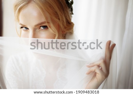 Blonde beauty woman in a white dress stands at the window. High quality photo