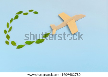Selective focus of wooden airplane model emitting fresh green leaves on blue background. Sustainable travel; clean and green energy; and biofuel for aviation industry concept. Royalty-Free Stock Photo #1909483780