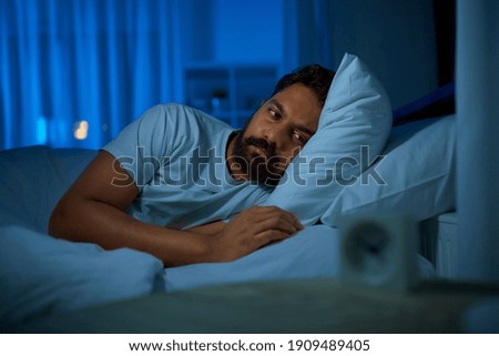 sleeping, insomnia and people concept - sleepless indian man lying in bed at home at night Royalty-Free Stock Photo #1909489405