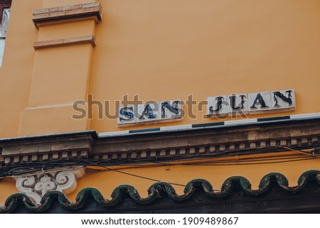 Street name sign on a side of a building on San Juan in Seville, Andalusia, Spain. 