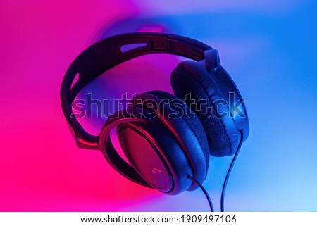 Stylish black wireless headphones lit with colorful neon light on abstract background isolated. Modern technology concept with copy space