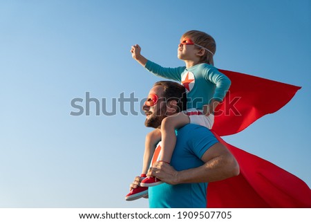 Family of superheroes having fun outdoor. Father and son playing against blue summer sky background. Imagination and freedom concept