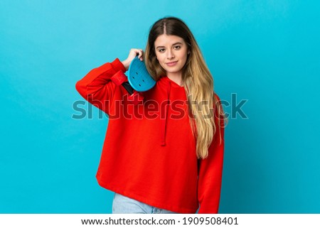 Young blonde woman isolated on blue background with a skate