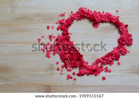 red cut paper sprinkles formed into the shape of a heart on wood