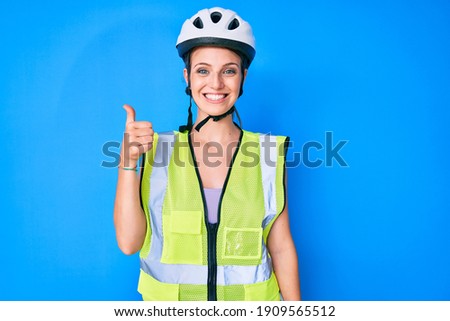 Young caucasian girl wearing bike helmet and reflective vest smiling happy and positive, thumb up doing excellent and approval sign 