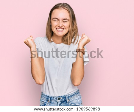 Beautiful young blonde woman wearing casual white t shirt excited for success with arms raised and eyes closed celebrating victory smiling. winner concept. 