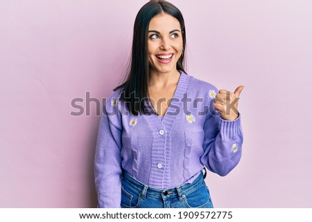 Young brunette woman wearing spring cardigan with flowers print pointing thumb up to the side smiling happy with open mouth  Royalty-Free Stock Photo #1909572775