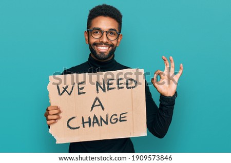 Young african american man holding we need a change banner doing ok sign with fingers, smiling friendly gesturing excellent symbol 