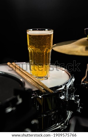 Glass of light beer on professional drum set closeup. Drumsticks, drums and cymbals, at live music rock concert, in the club stage, bar, or in recording studio. Black background.