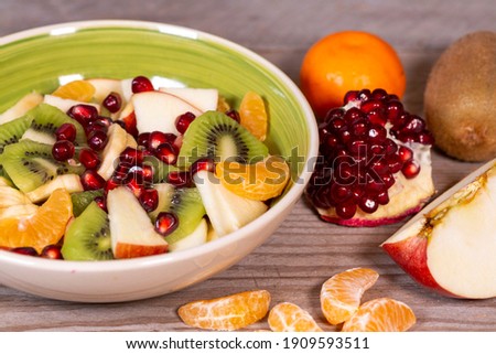 Fruit salad in a ceramic bowl and various fruits on a wooden table. Superfood, vegetarian food, healthy lifestyle.  Royalty-Free Stock Photo #1909593511